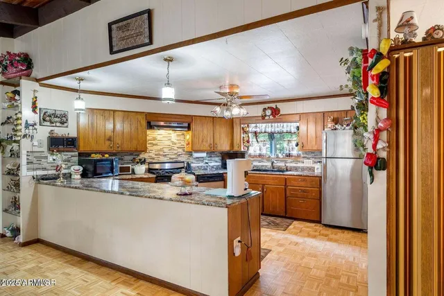 a kitchen with stainless steel appliances granite countertop a refrigerator a sink dishwasher a stove top oven a dining table and chairs with wooden floor