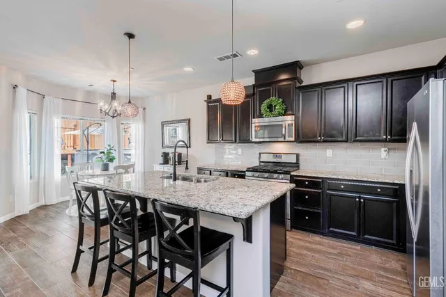 a kitchen with stainless steel appliances granite countertop a stove top oven a sink dishwasher a dining table and chairs with wooden floor