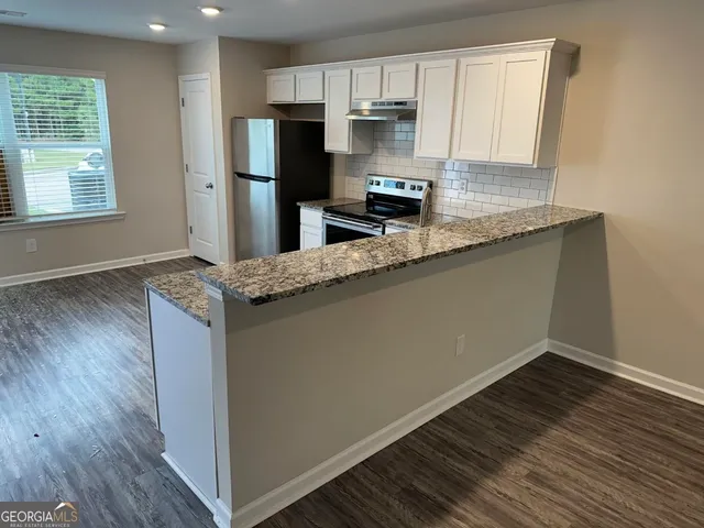 a kitchen with stainless steel appliances granite countertop a refrigerator a sink a stove and wooden floors