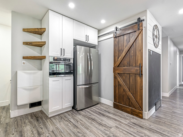 523 South Main Street Payson, UT 84651 - Photo 13 of 41 Kitchen area featuring wood-finish flooring, white cabinetry with modern hardware, stainless steel appliances, and a dark wood barn door on a black track