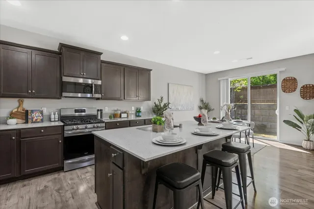 a kitchen with stainless steel appliances granite countertop a stove a sink dishwasher a microwave oven and a dining table with wooden cabinet