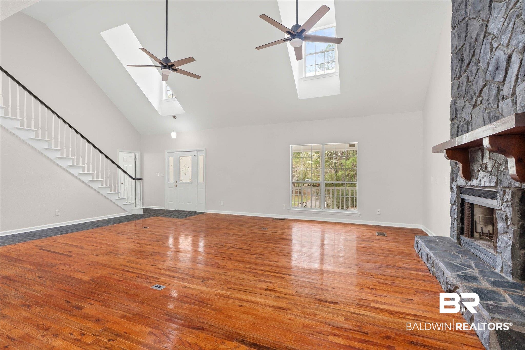 106 Melanie Loop Daphne, AL 36526 - Photo 7 of 45 Unfurnished living room with a skylight, hardwood / wood-style floors, a stone fireplace, vaulted ceiling, and ceiling fan