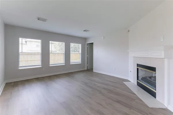 an empty room with wooden floor fireplace and windows
