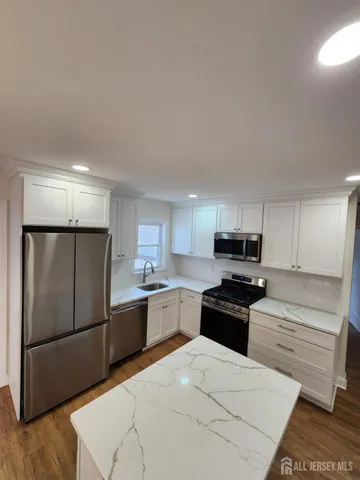a kitchen with stainless steel appliances kitchen island granite countertop a refrigerator sink and white cabinets
