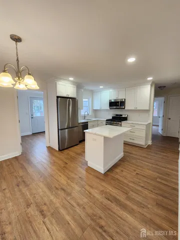 a large kitchen with kitchen island a sink dishwasher a refrigerator and a stove with wooden floor