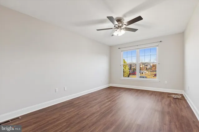 a view of an empty room with wooden floor and a fan