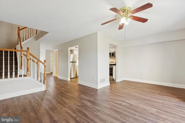 a view of an empty room with wooden floor and a ceiling fan