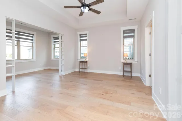 an empty room with wooden floor fan and windows