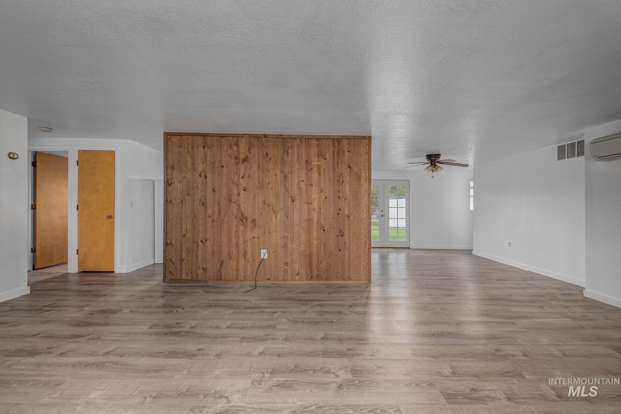 4484 Community Road Ontario, OR 97914 - Photo 6 of 35 Unfurnished living room with light wood-style floors, a textured ceiling, wood walls, a ceiling fan, and french doors