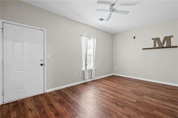 an empty room with wooden floor chandelier fan and windows