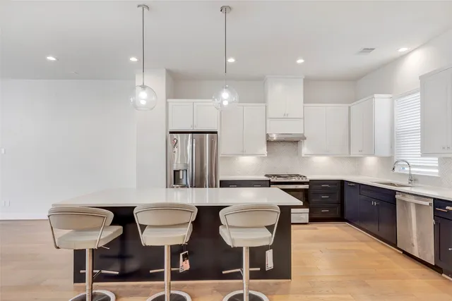 a kitchen with stainless steel appliances kitchen island granite countertop a refrigerator a sink dishwasher a stove and white cabinets with wooden floor