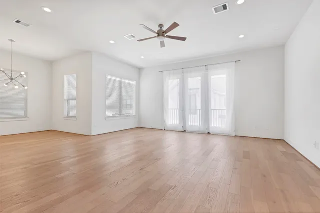an empty room with wooden floor fan and windows