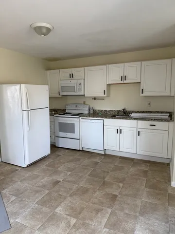 a kitchen with granite countertop a sink a stove a refrigerator and white cabinets