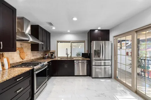 a kitchen with stainless steel appliances kitchen island granite countertop a table chairs and a refrigerator