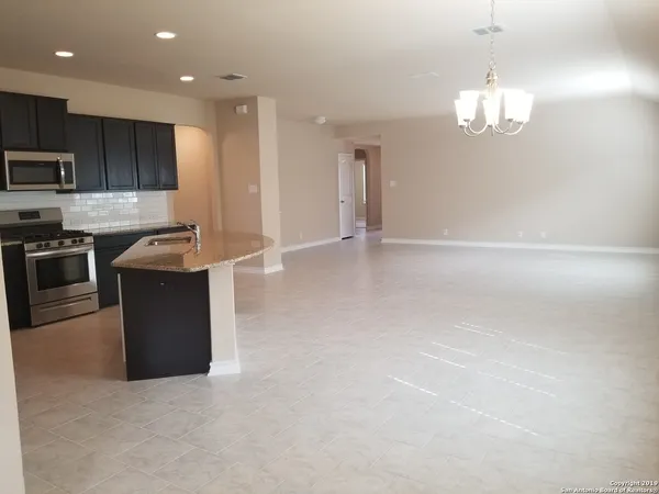 a kitchen with stainless steel appliances granite countertop a stove top oven a sink dishwasher a refrigerator and a dining table with wooden floor