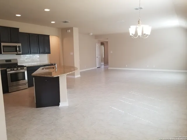 a kitchen with stainless steel appliances granite countertop a stove top oven a sink dishwasher a refrigerator and a dining table with wooden floor