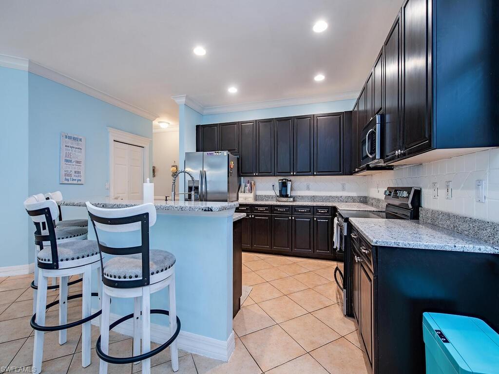 2346 Butterfly Palm Drive Naples, FL 34119 - Photo 5 of 45 Kitchen with appliances with stainless steel finishes, a breakfast bar, light tile patterned floors, ornamental molding, and an island with sink