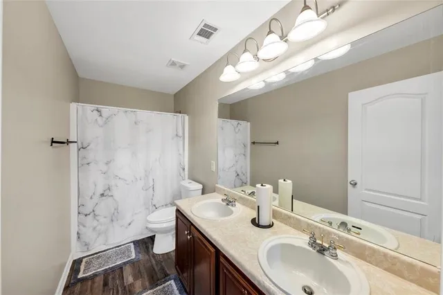 a bathroom with double vanity sink a toilet a shower and a mirror