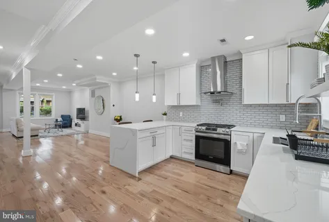 a large white kitchen with stainless steel appliances granite countertop a stove a sink a refrigerator and white cabinets