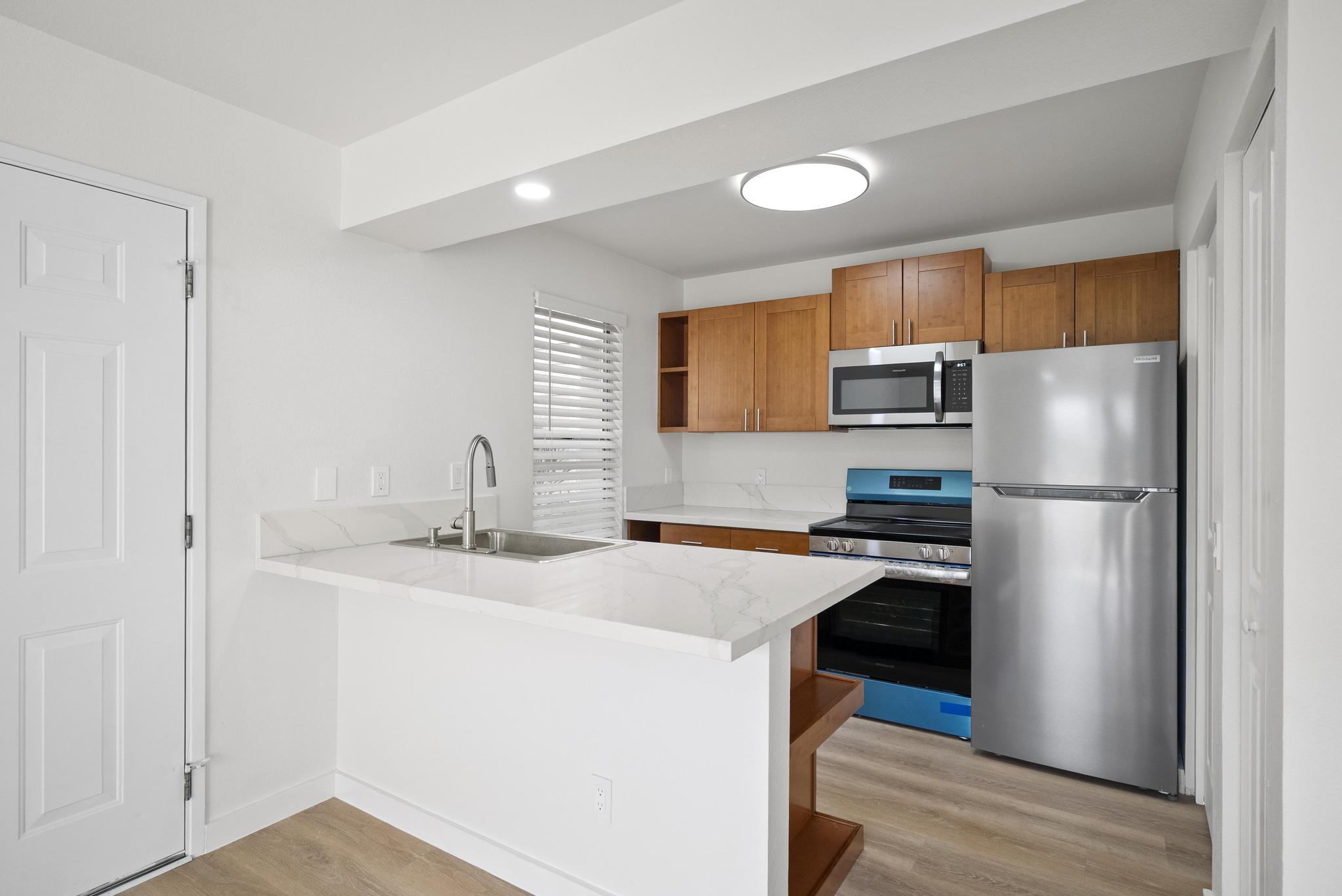68-3831 Lua Kula Street, Unit E102 Waikoloa, HI 96738 - Photo 2 of 26 a kitchen with stainless steel appliances granite countertop a refrigerator a sink a stove and white cabinets with wooden floor