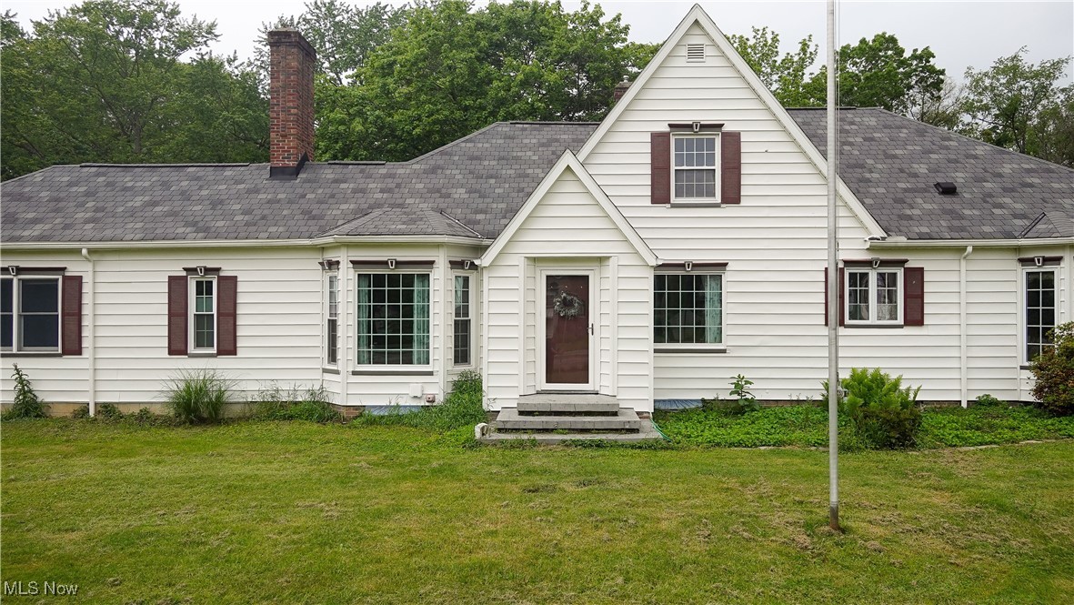 View of front of home with a front yard, a chimney, and a shingled roof