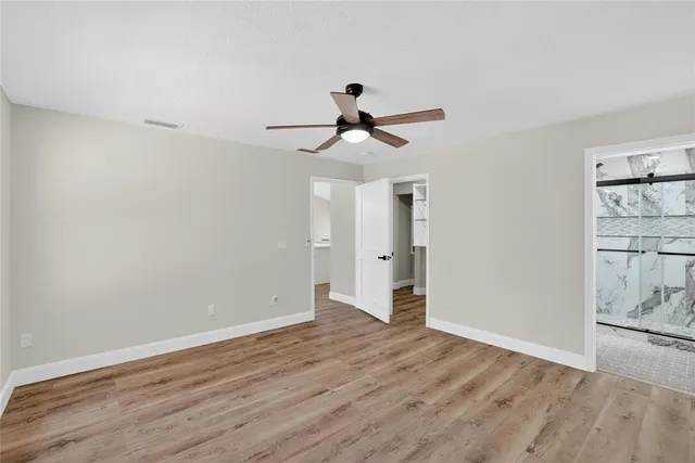 an empty room with wooden floor chandelier fan and windows