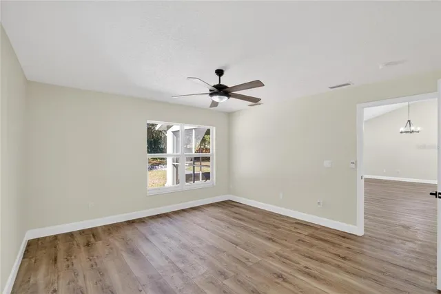 an empty room with wooden floor fan and windows