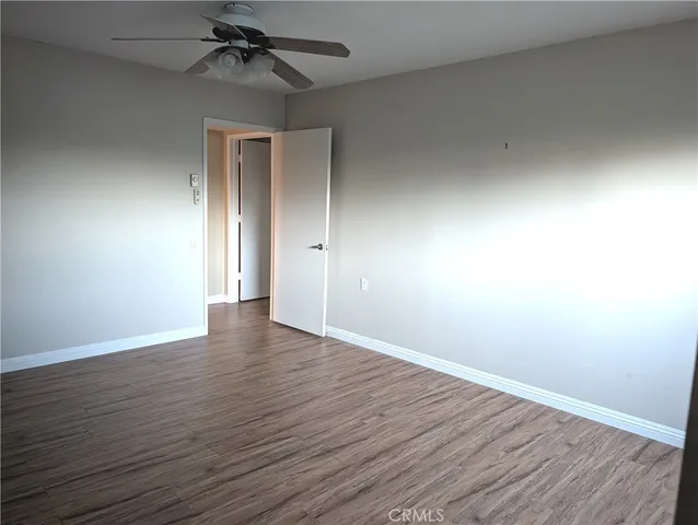 a view of an empty room with wooden floor and a ceiling fan