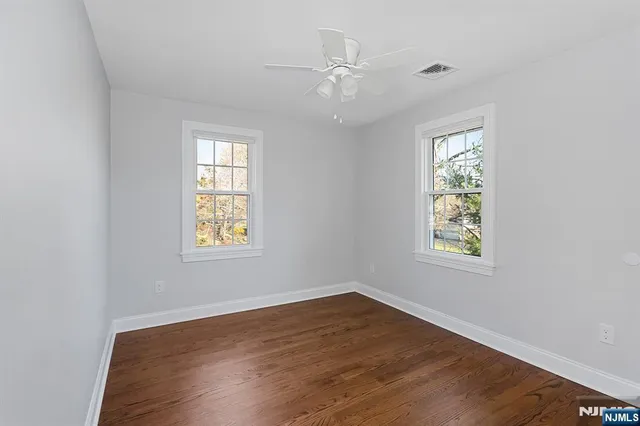 an empty room with wooden floor windows and fan