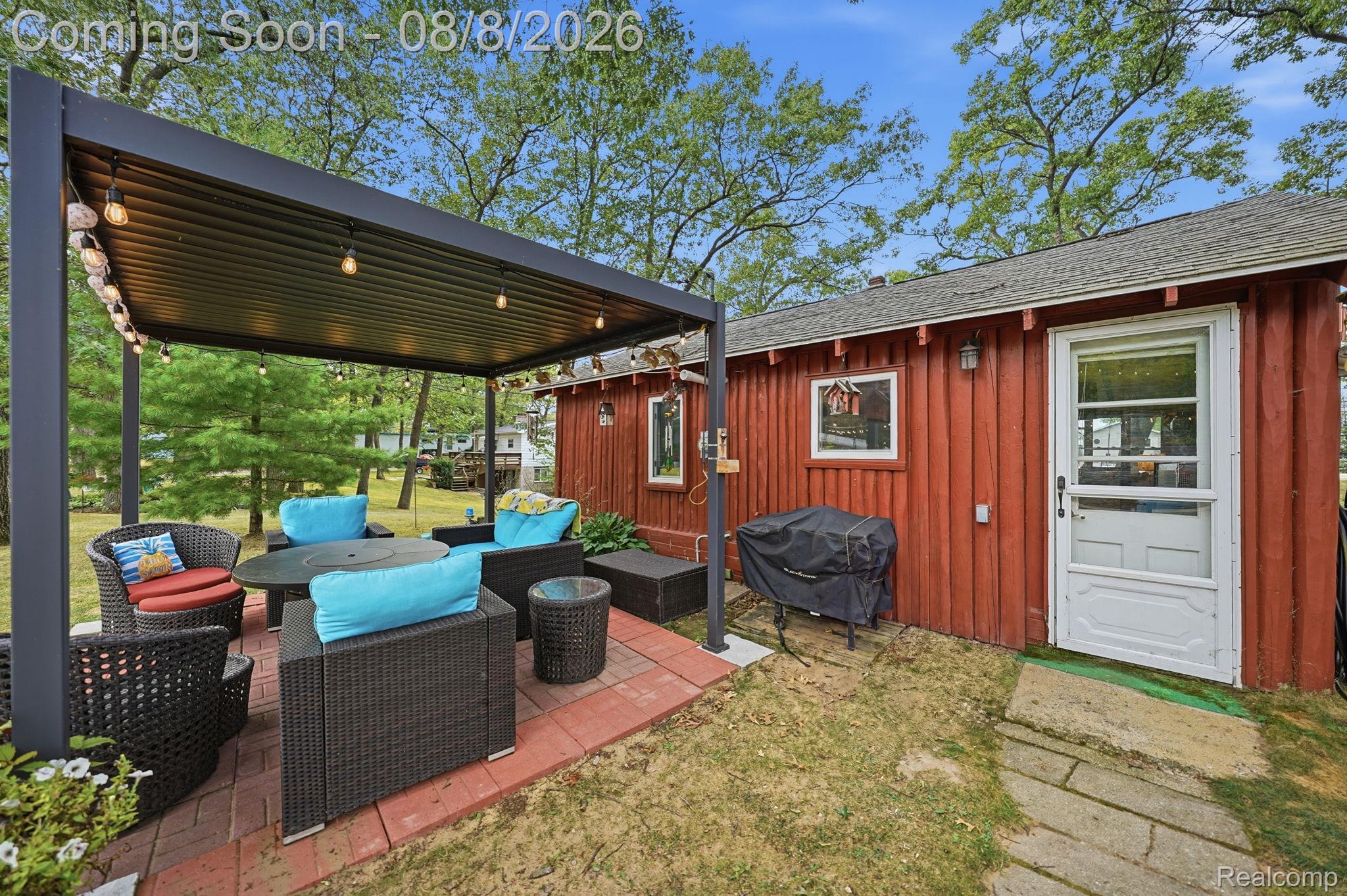4599 Port Austin Road Caseville, MI 48725 - Photo 26 of 40 Red vertical plank siding, white storm door, white window trim, brick paver patio, and modern black pergola