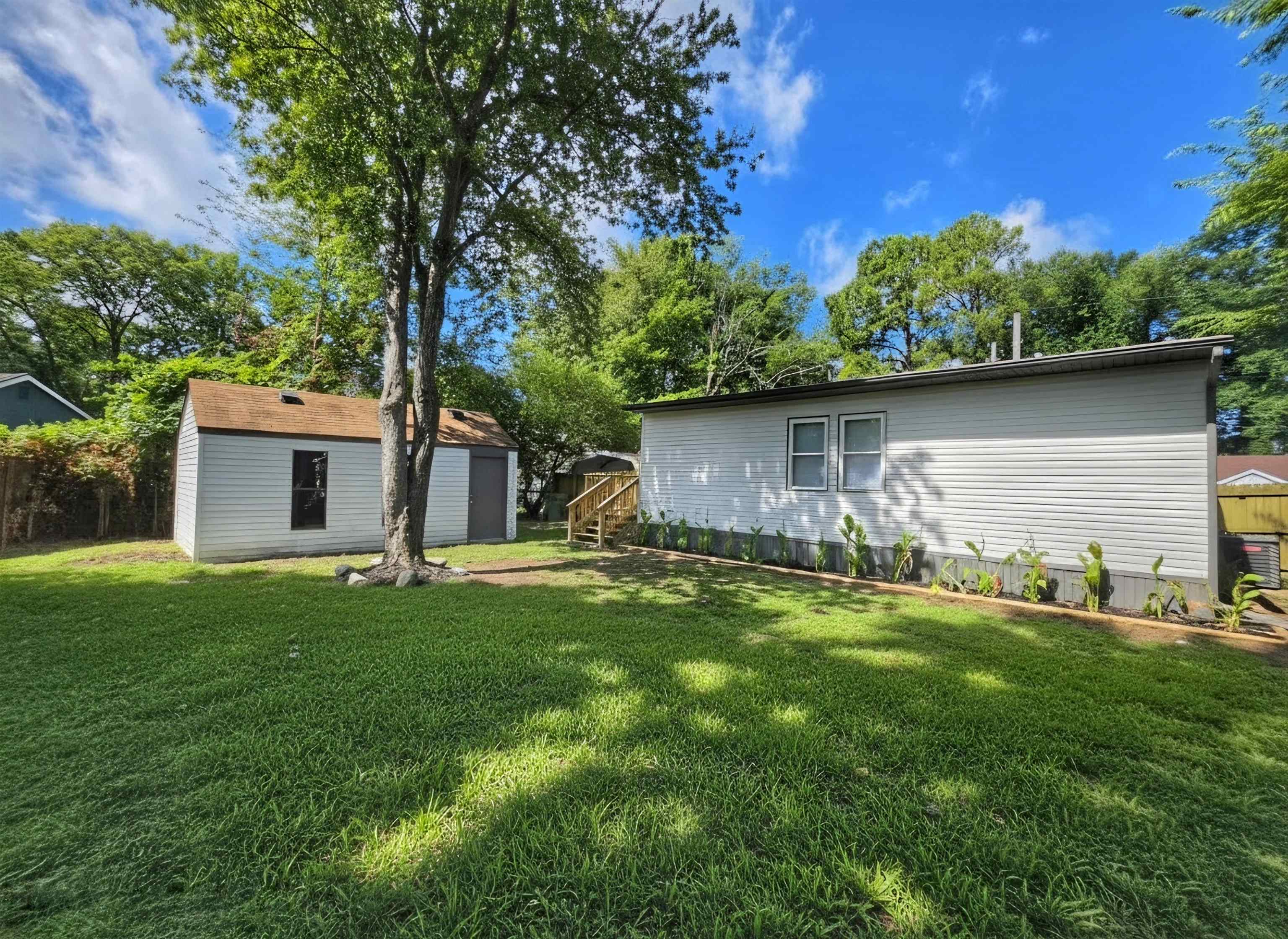 7966 Martha Road Millington, TN 38053 - Photo 25 of 26 Spacious green lawn featuring a mature tree, a detached storage shed with a brown roof, and the property's exterior with white siding and a wood deck