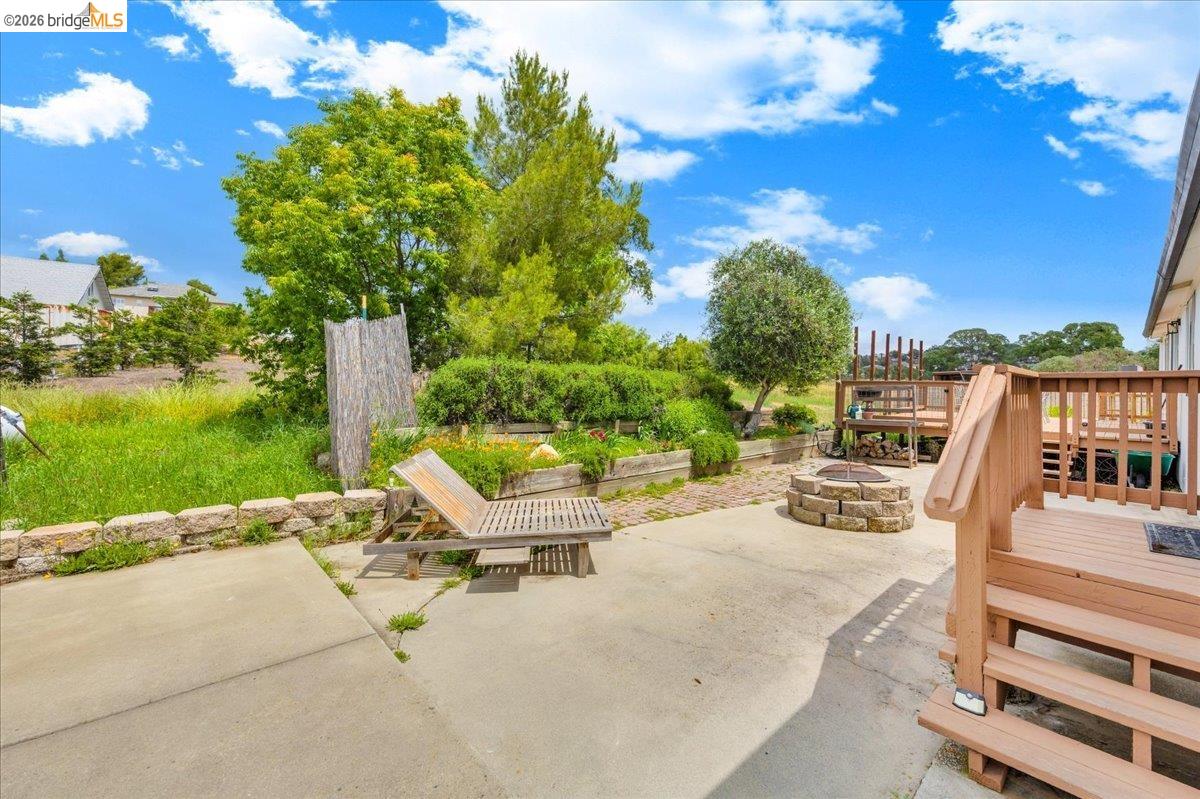 4419 Little John Road Copperopolis, CA 95228 - Photo 27 of 43 Expansive concrete patio featuring a stone-clad fire pit, raised garden beds with stone retaining walls, and a multi-level wood deck