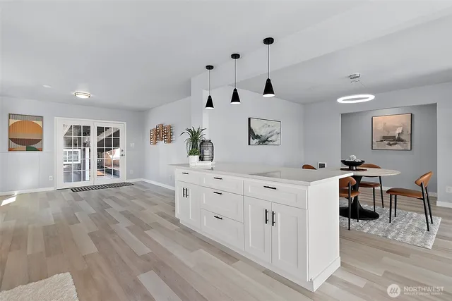 a large white kitchen with stainless steel appliances kitchen island a stove a refrigerator a dining table and chairs with wooden floor