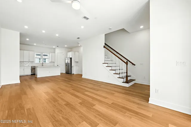 a view of an empty room and kitchen with wooden floor