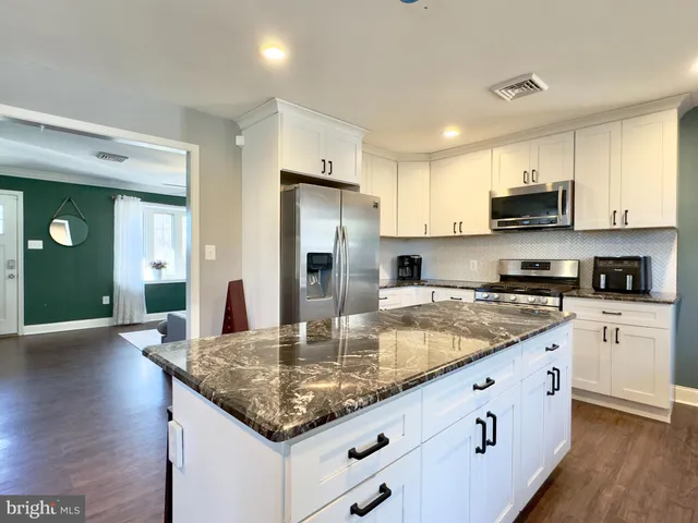 a kitchen with granite countertop a stove top oven a sink dishwasher a refrigerator and white cabinets with wooden floor