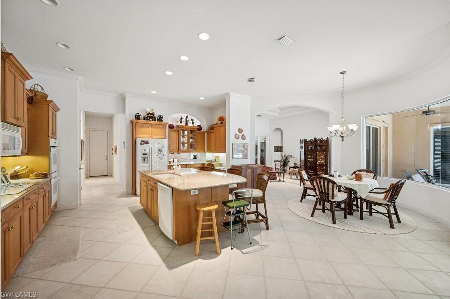 7488 Treeline Drive Naples, FL 34119 - Photo 8 of 22 Kitchen with arched walkways, white appliances, a breakfast bar, brown cabinetry, and a center island with sink