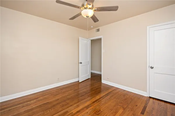 an empty room with wooden floor chandelier fan and windows