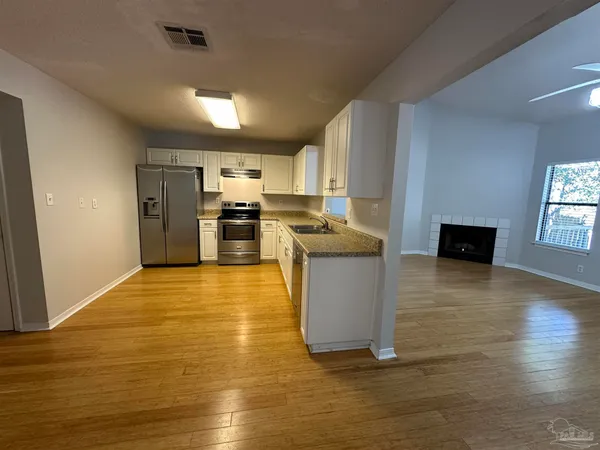 a kitchen with stainless steel appliances granite countertop a stove top oven a sink dishwasher a refrigerator and white cabinets with wooden floor