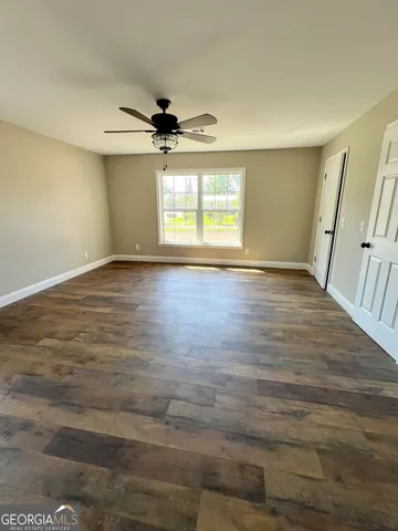 an empty room with wooden floor ceiling fan and windows