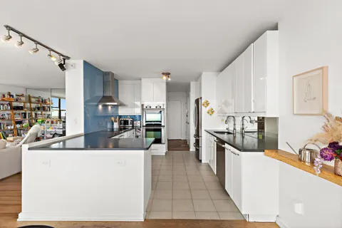 a large kitchen with stainless steel appliances a refrigerator a stove top oven a sink dishwasher and white cabinets next to a window