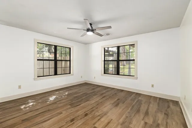an empty room with wooden floor ceiling fan and windows