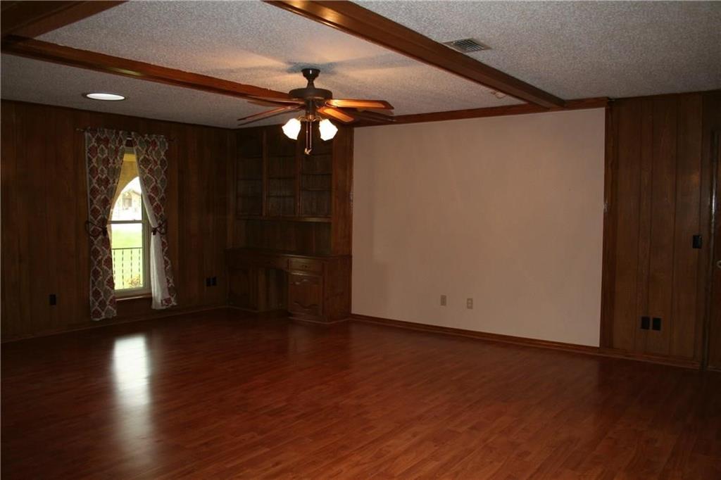 2107 Forest Grove Estates Road Allen, TX 75002 - Photo 6 of 13 Unfurnished living room with beamed ceiling, a ceiling fan, wooden walls, wood finished floors, and a textured ceiling