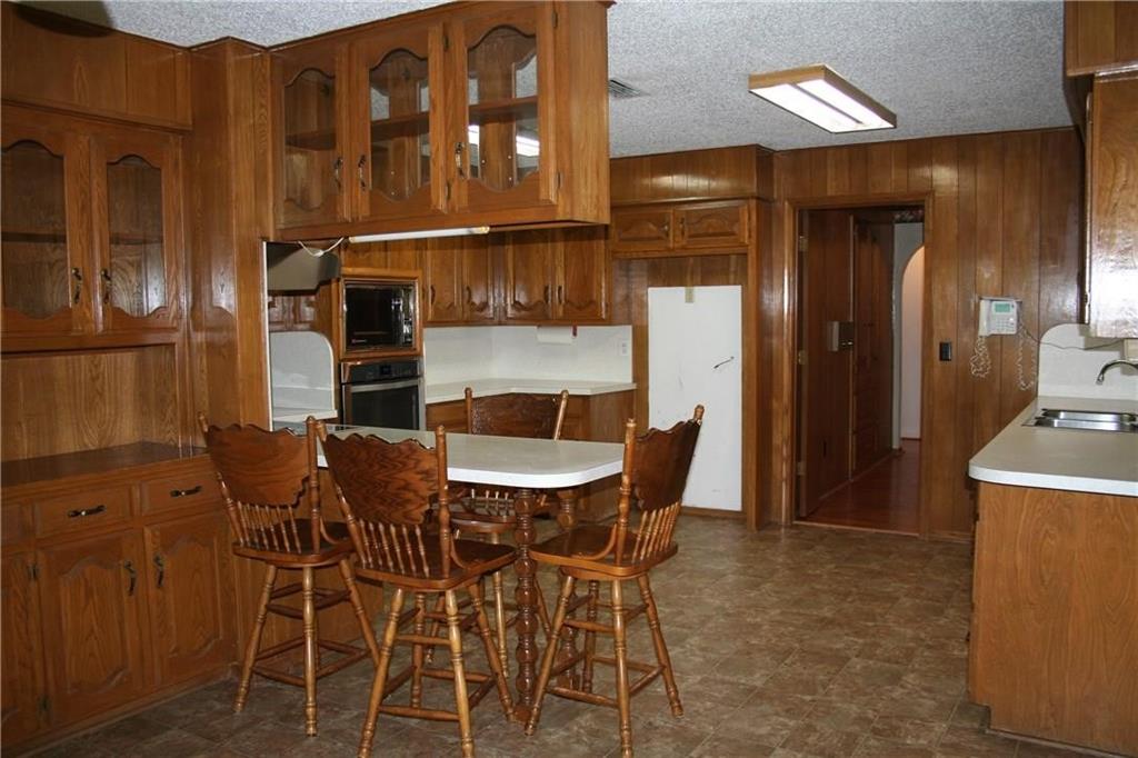 2107 Forest Grove Estates Road Allen, TX 75002 - Photo 9 of 13 Kitchen with wooden walls, brown cabinetry, glass insert cabinets, arched walkways, and stainless steel oven