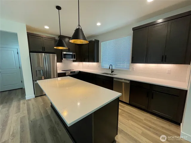 a kitchen with stainless steel appliances a sink a wooden floor cabinets and a chandelier