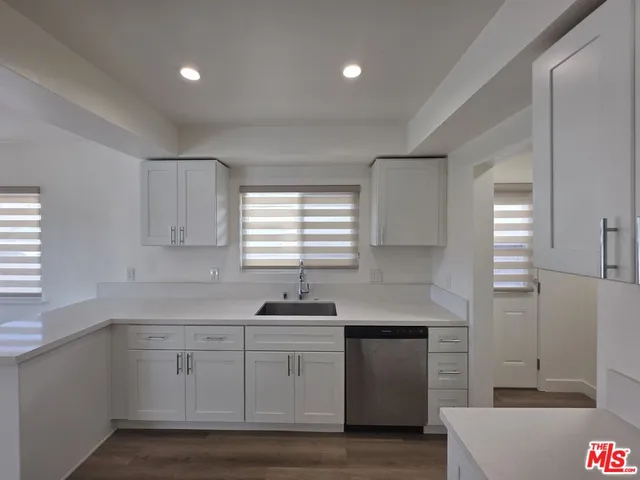 a kitchen with granite countertop a refrigerator a sink dishwasher a stove and white countertops with wooden floor