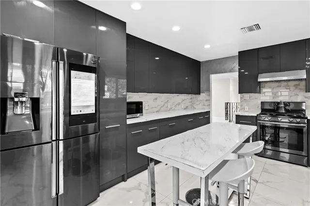 a kitchen with stainless steel appliances kitchen island granite countertop a refrigerator a stove a sink a microwave with white cabinets and wooden floor