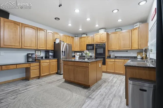 a kitchen with stainless steel appliances granite countertop wooden cabinets a refrigerator a sink a stove a microwave and wooden floors