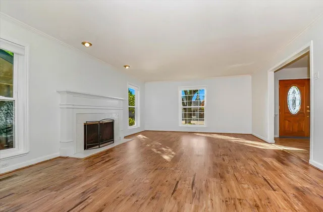 an empty room with wooden floor fireplace and windows