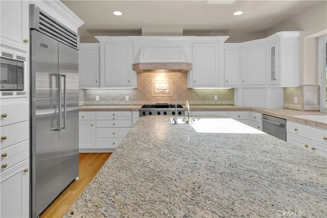 a kitchen with stainless steel appliances granite countertop a stove top oven a sink dishwasher and a refrigerator with wooden floor