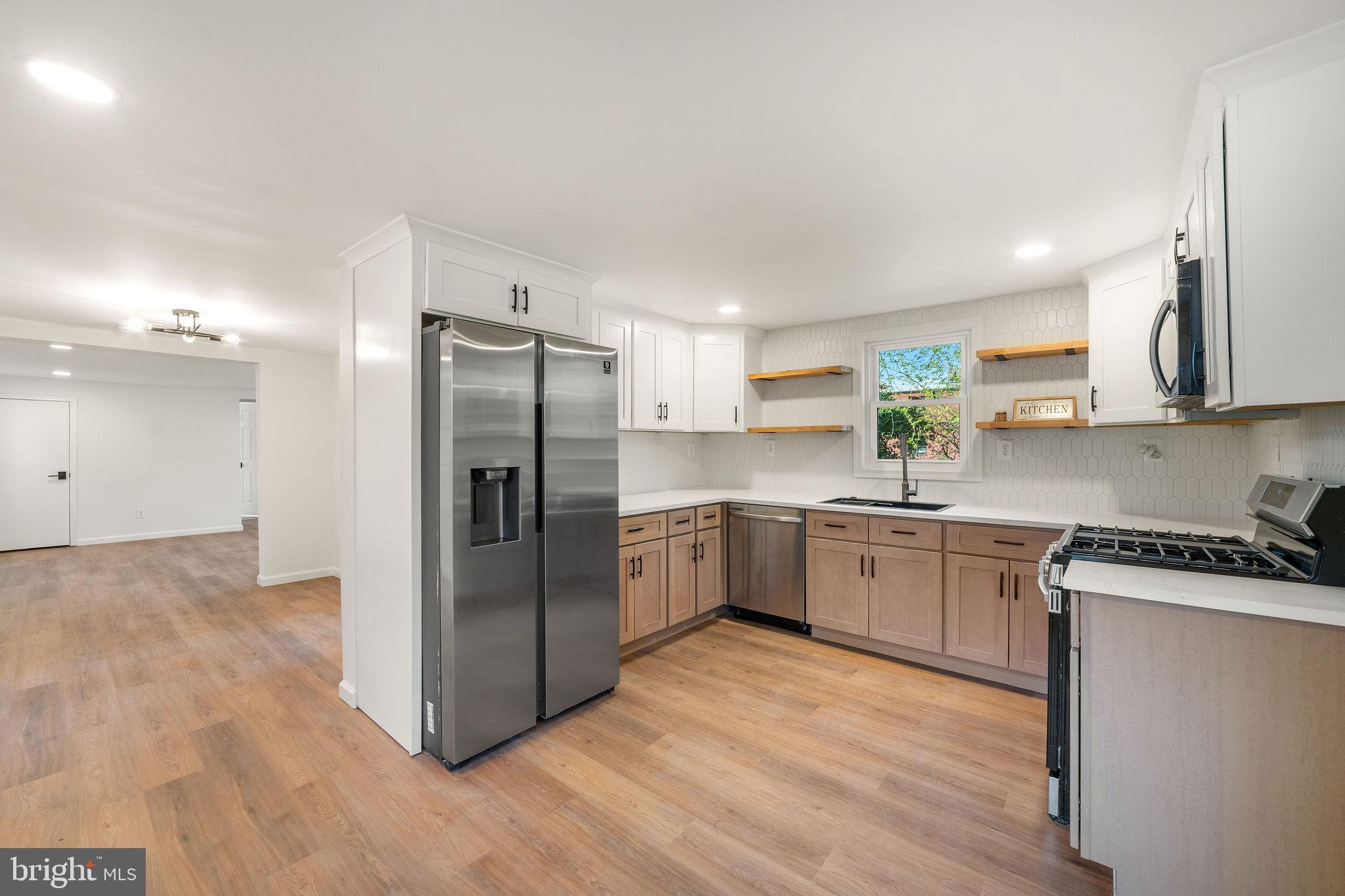 a kitchen with stainless steel appliances granite countertop a refrigerator a sink dishwasher a stove and white countertops with wooden floor